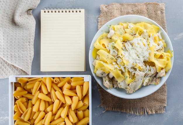 Harina de pasta con cuaderno, pasta cruda, papel de cocina en un plato