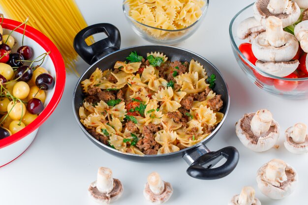 Harina de pasta con pasta cruda, champiñones, tomate, cereza en una sartén