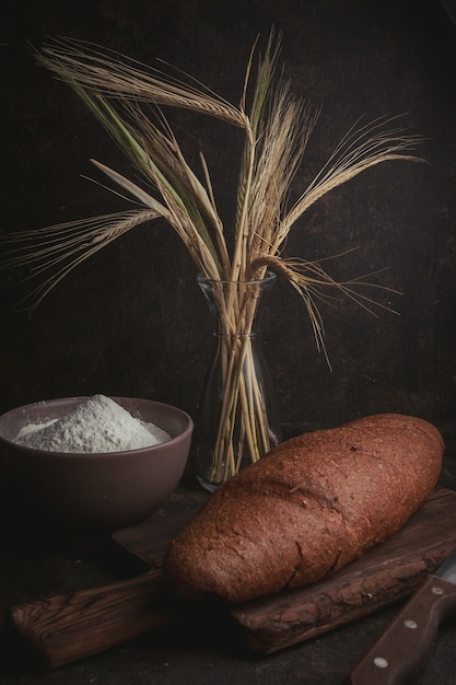Harina en un tazón con trigo y pan vista lateral en un marrón oscuro