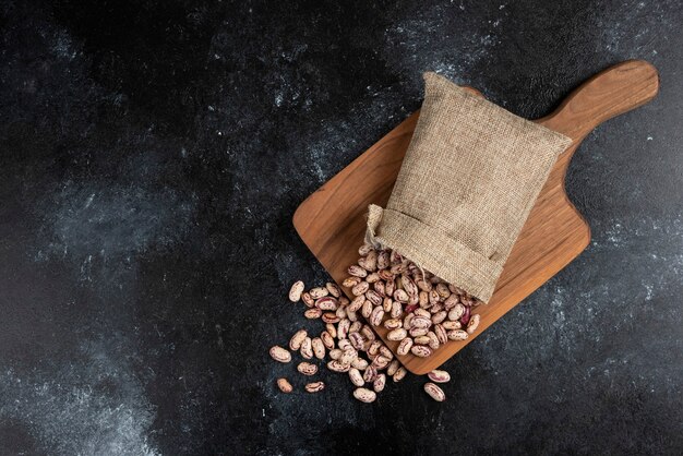 Harpillera de frijoles crudos secos colocados sobre tabla de madera.