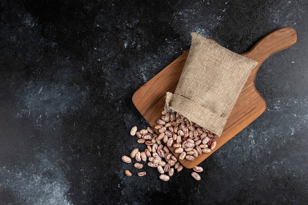 Harpillera de frijoles crudos secos colocados sobre tabla de madera.