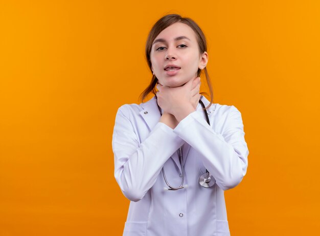 Harto de la joven doctora vistiendo una bata médica y un estetoscopio ahogándose en un espacio naranja aislado con espacio de copia