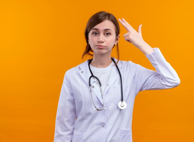 Harto de la joven doctora vistiendo una bata médica y un estetoscopio haciendo gesto de suicidio en un espacio naranja aislado con espacio de copia