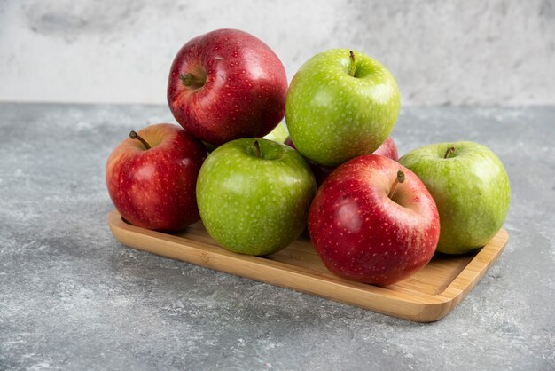 Hay un montón de manzanas verdes y rojas frescas colocadas en un plato de madera.