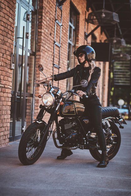 Hay una mujer madura sexy con gafas de sol y casco protector negro en su moto.