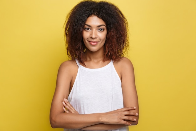 Foto gratuita headshot retrato de hermosa mujer afroamericana atractiva posting cruzó los brazos con sonrisa feliz. fondo amarillo del estudio. espacio de la copia.