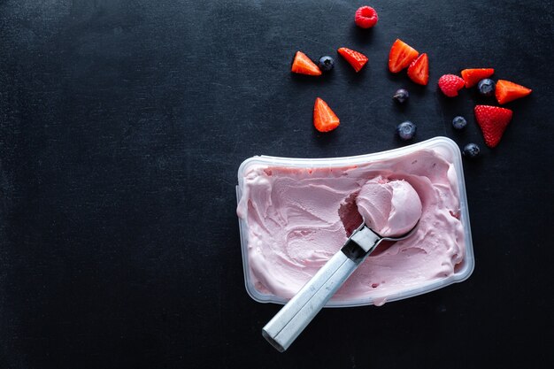 Helado casero de frutos rojos con cuchara de helado en un recipiente.