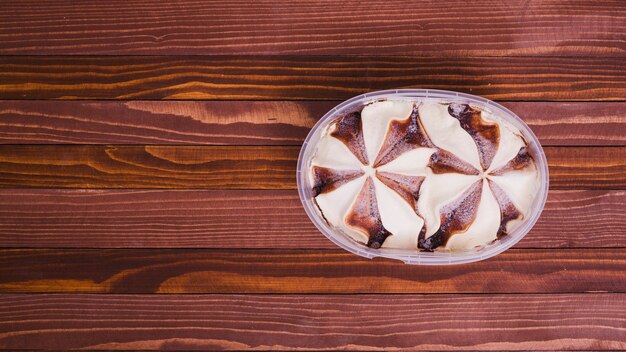 Helado con chocolate en un recipiente de plástico en la mesa de madera