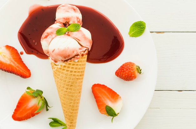 Helado en cono de waffle con sirope de fresa.