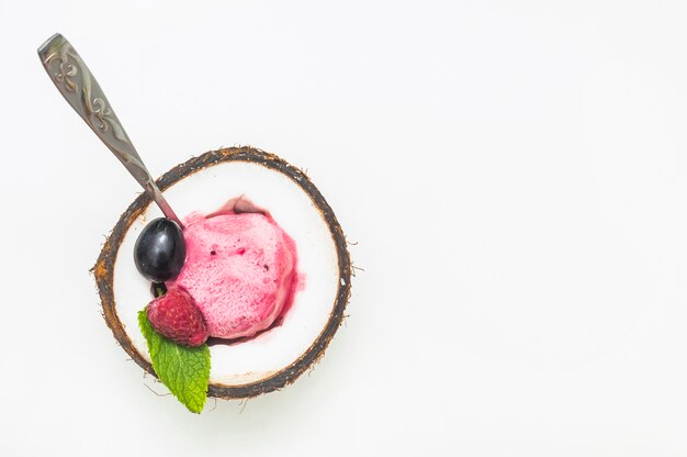 Helado de frambuesa dentro de la mitad del coco con una cuchara contra el fondo blanco