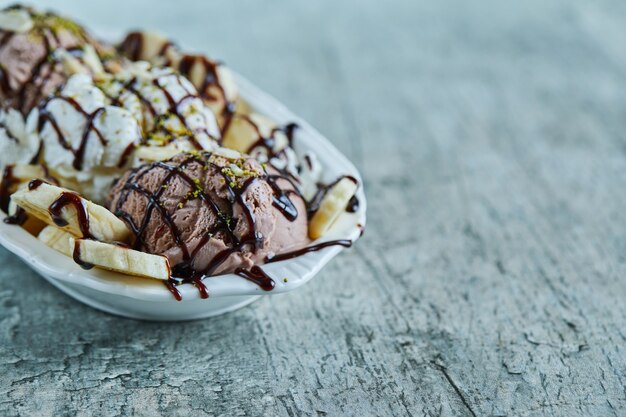 Helado con plátanos, chocolate y chispitas en la placa blanca.