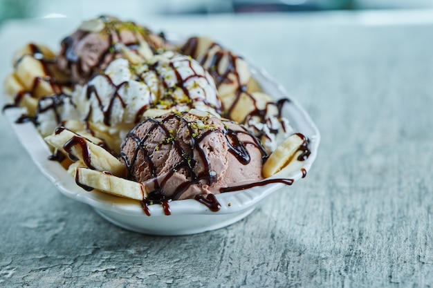 Helado con plátanos, chocolate y chispitas en la placa blanca.