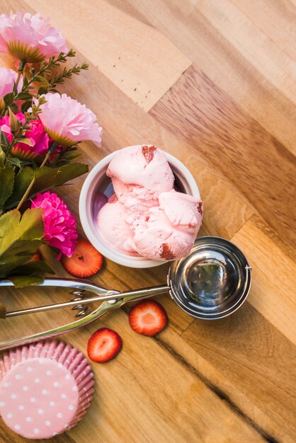 Helado rosado en un tazón cerca de la cucharada con rebanadas de bayas frescas y flores