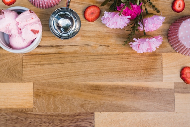 Helado en un tazón cerca de la cucharada con rodajas de bayas frescas y flores