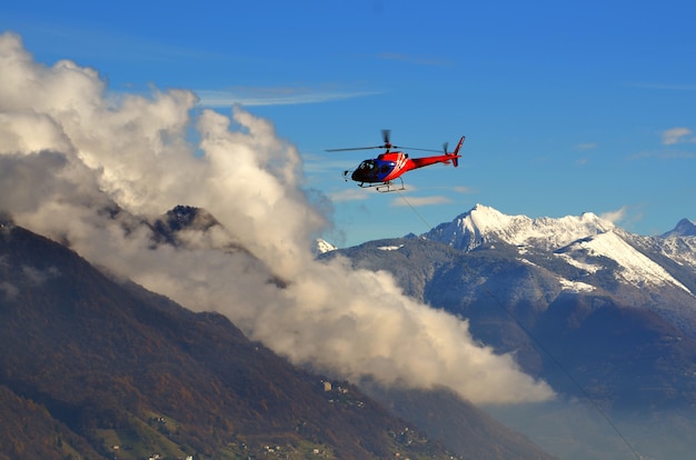 Helicóptero volando entre las nubes sobre las montañas nevadas