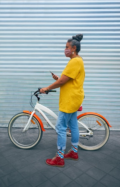 Hembra adulta vistiendo ropas coloridas y de pie contra la puerta de un garaje con una bicicleta