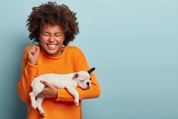 Hembra afro feliz aprieta el puño de alegría, feliz de comprar un perro de raza de pedigrí deseable