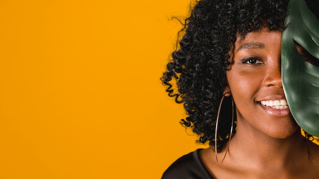 Hembra afroamericana joven sonriente con la hoja en fondo coloreado