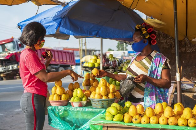 Hembra afroamericana en una mascarilla protectora de compras en un mercado de frutas