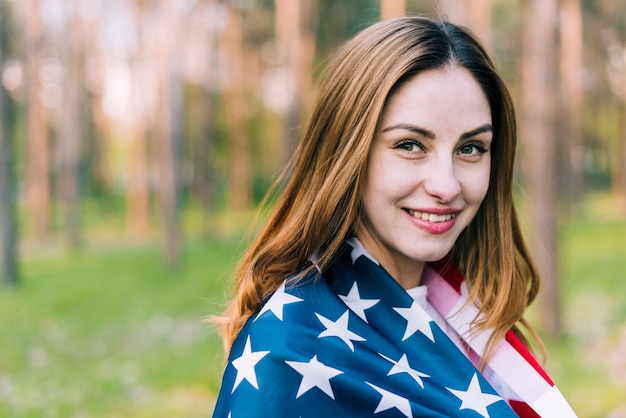 Foto gratuita hembra alegre que lleva la bandera de los eeuu en hombros