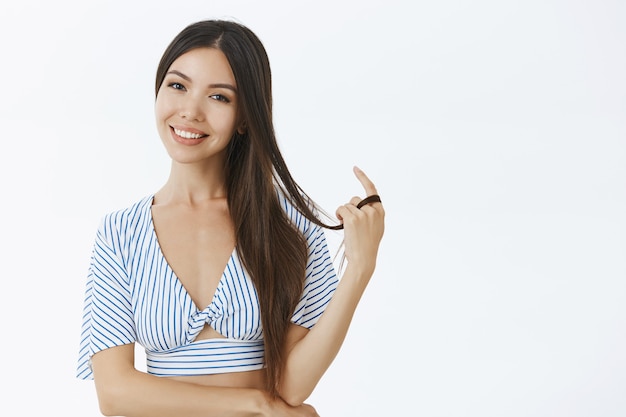 Foto gratuita hembra con blusa de rayas recortadas jugando con un mechón de cabello y sonriendo alegremente coqueteando durante la charla