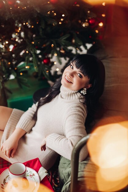 Hembra feliz en un árbol de Navidad girando su cara sonriente a la cámara