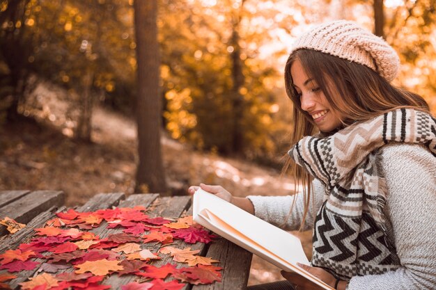 Hembra joven alegre leyendo en la mesa en el parque