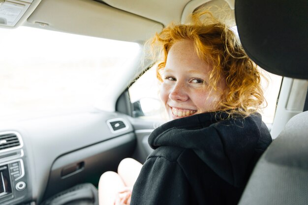 Hembra joven alegre que se sienta en coche