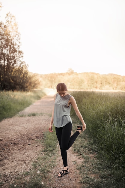 Hembra joven atleta estirando su pierna en el campo rural