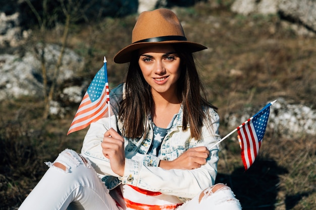 Foto gratuita hembra joven atractiva que se sienta con las banderas americanas en la naturaleza