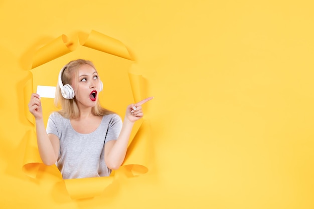 Hembra joven en auriculares con tarjeta de crédito en la pared amarilla