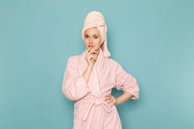 Hembra joven en bata de baño rosa después de la ducha posando en azul