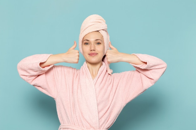 Hembra joven en bata de baño rosa después de la ducha sonriendo y mostrando como signo en azul