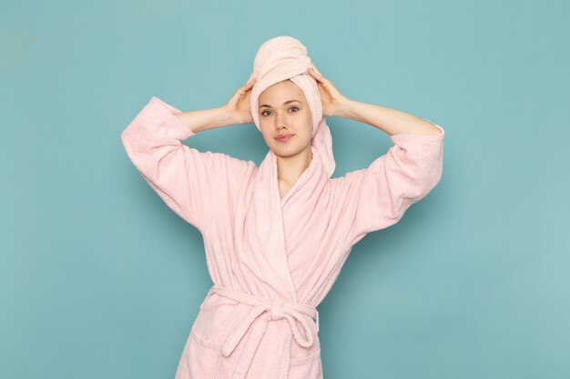 Hembra joven en bata de baño rosa después de la ducha sonriendo y posando en azul