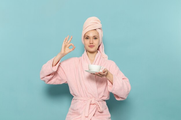 Hembra joven en bata de baño rosa después de la ducha sosteniendo una taza de café en azul