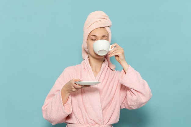 Hembra joven en bata de baño rosa después de la ducha tomando café en azul