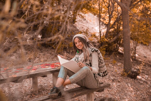 Hembra joven con buen libro en el parque de otoño