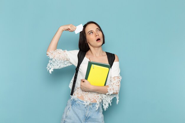 Hembra joven en camisa blanca, blue jeans y bolso negro sosteniendo cuadernos en azul