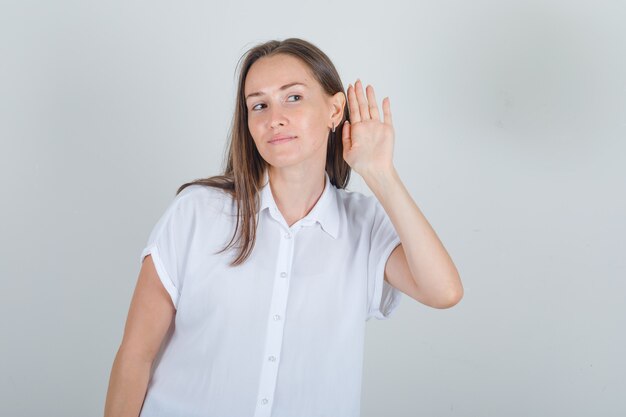 Hembra joven en camisa blanca de la mano a la oreja