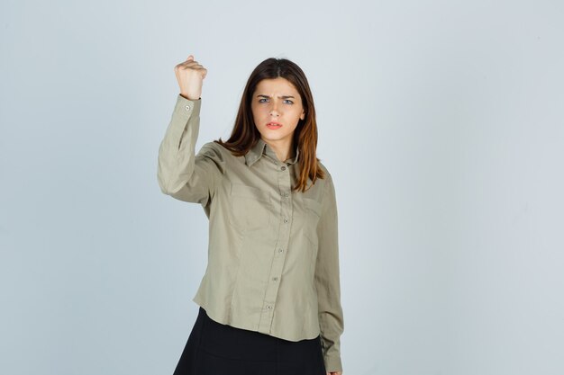 Hembra joven en camisa, falda levantando el puño cerrado y mirando rencoroso