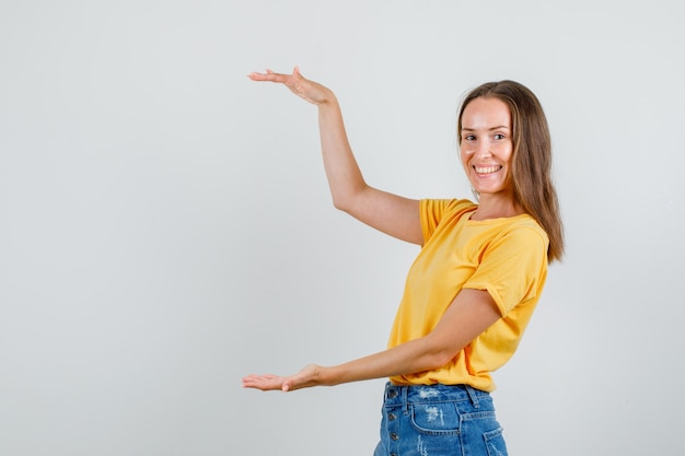 Foto gratuita hembra joven en camiseta, pantalones cortos que muestran un cartel de gran tamaño y un aspecto alegre