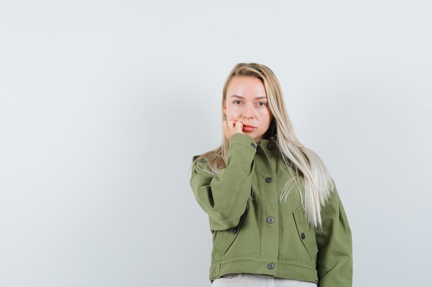 Hembra joven en chaqueta verde, jeans se centra en la cámara, vista frontal.