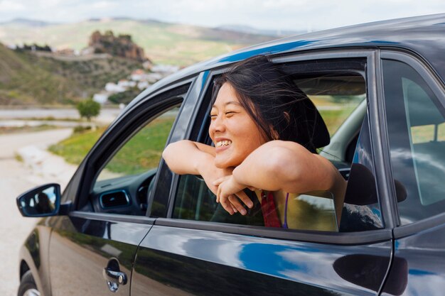 Hembra joven china alegre que mira la naturaleza de la ventana de coche