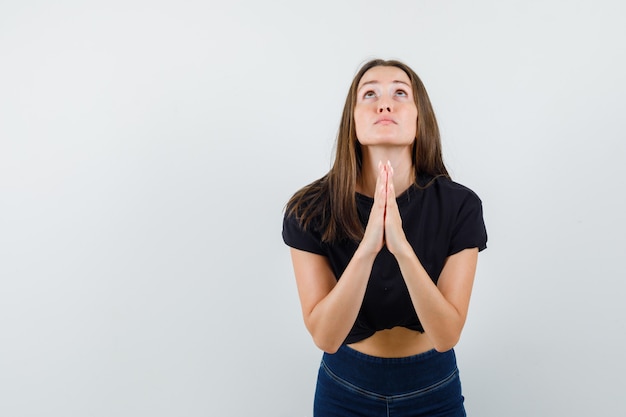 Foto gratuita hembra joven cogidos de la mano en gesto de oración en blusa negra, pantalones y mirando esperanzado
