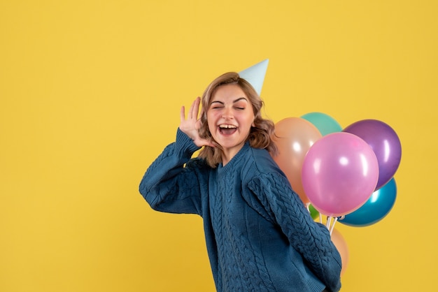 Hembra joven escondiendo globos de colores detrás de su espalda en amarillo