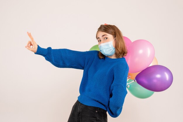 Hembra joven escondiendo globos de colores detrás de su espalda en blanco