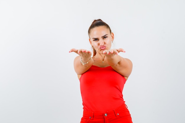 Foto gratuita hembra joven estirando las manos para dar algo en camiseta roja, pantalones y lucir linda. vista frontal.