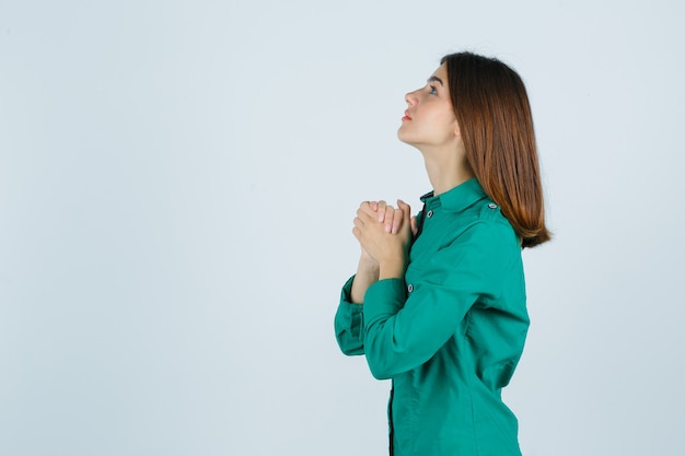 Foto gratuita hembra joven estrechando las manos en gesto de oración en camisa verde y mirando esperanzado.