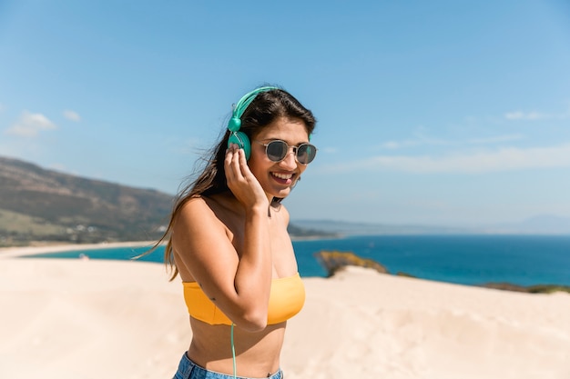 Hembra joven feliz que escucha la música en luz del sol en la costa