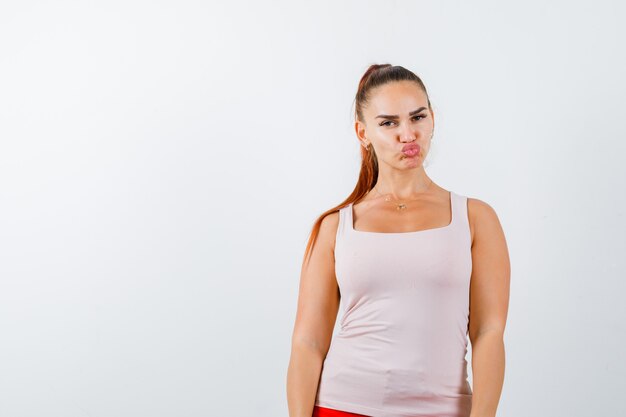 Hembra joven haciendo pucheros con los labios en camiseta y mirando confiado, vista frontal.